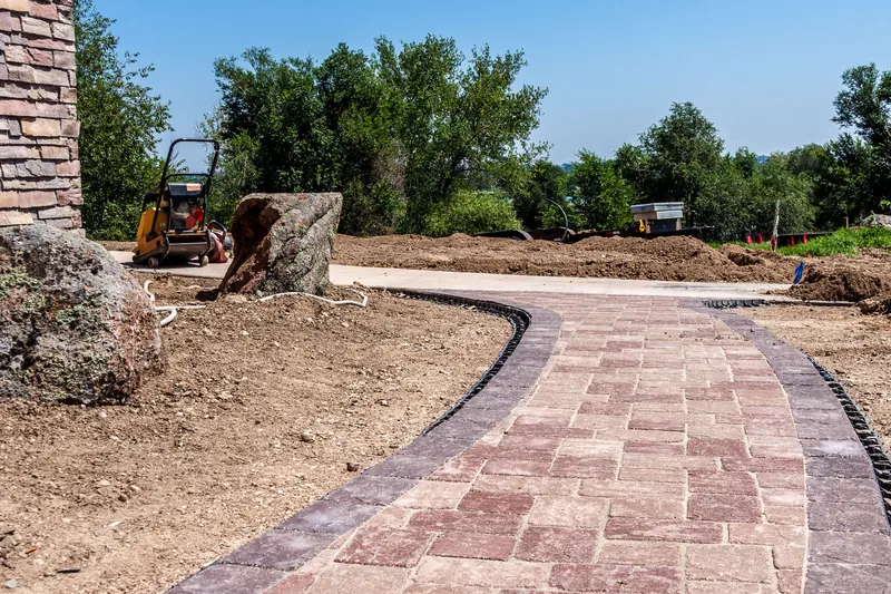 Curved paver path under construction with boulders nearby